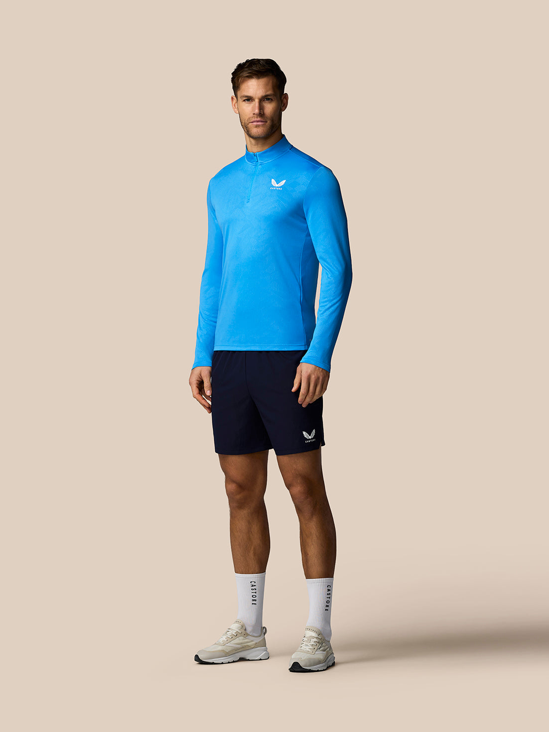 Man wearing a blue athletic long-sleeve shirt and black shorts on a beige background