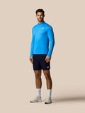 Man wearing a blue athletic long-sleeve shirt and black shorts on a beige background