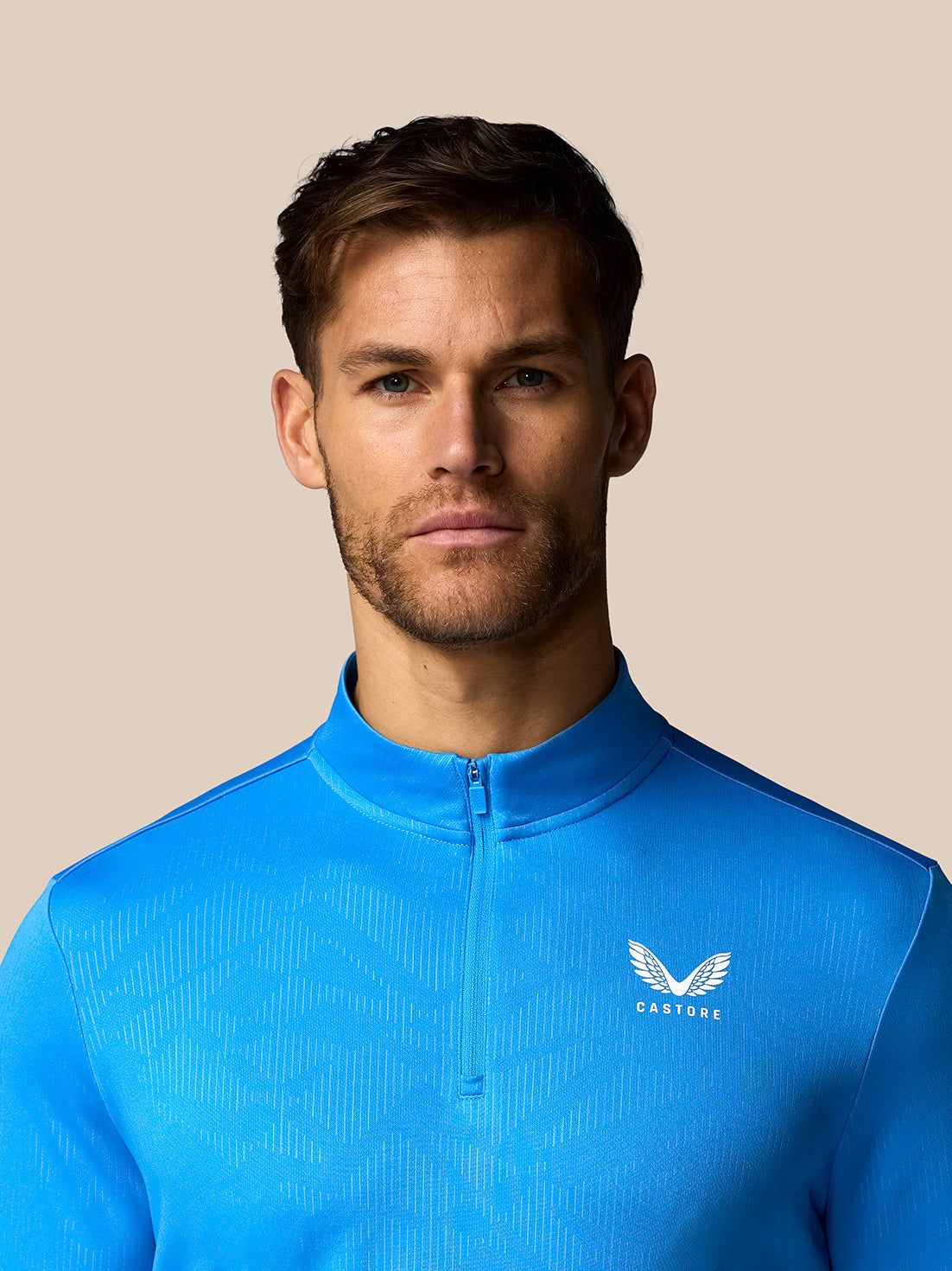 Man wearing a blue athletic jacket with a logo on a beige background