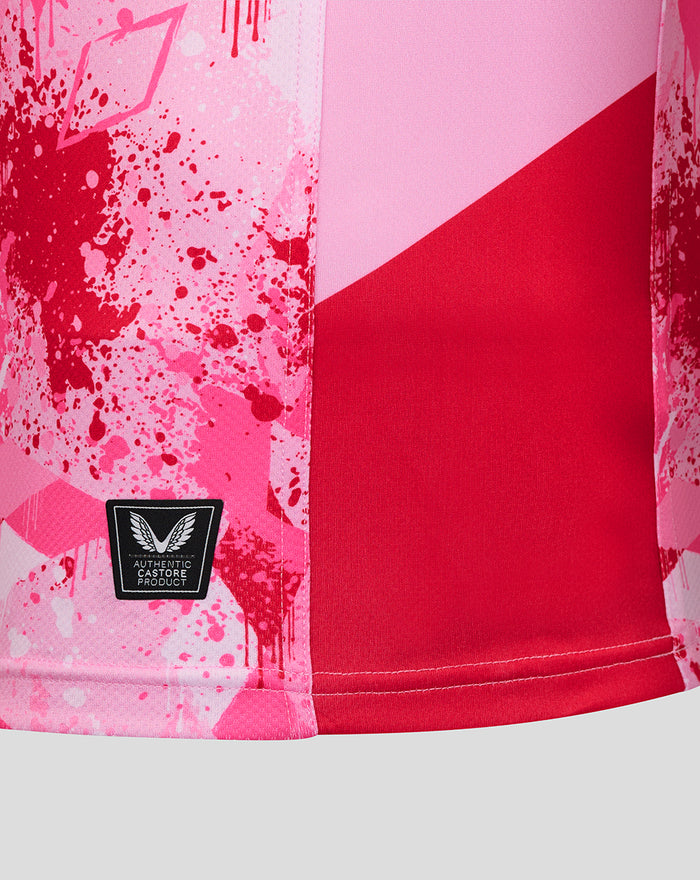 Close up of pink Harlequins away shirt hem showing red side panel and authentic Castore product badge