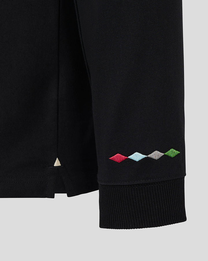 Close up of sleeve hem on black rugby shirt showing multicolor diamond embroidery near the cuff.