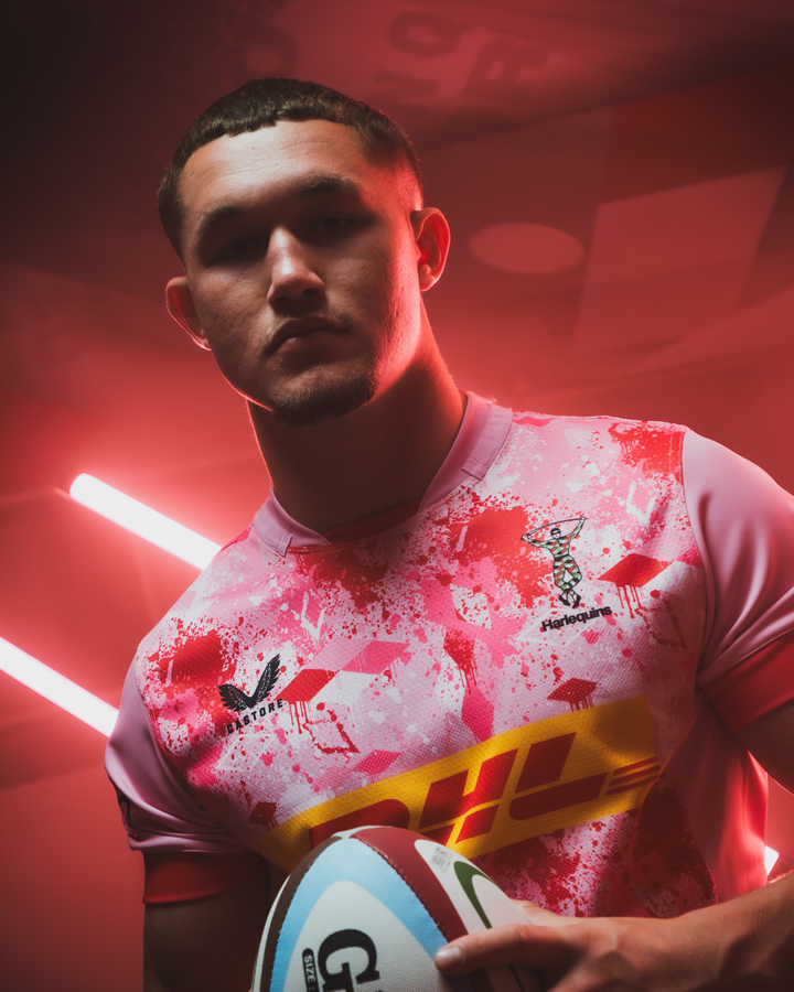 Male model wearing pink Harlequins away replica rugby shirt with splatter print and DHL sponsorship.